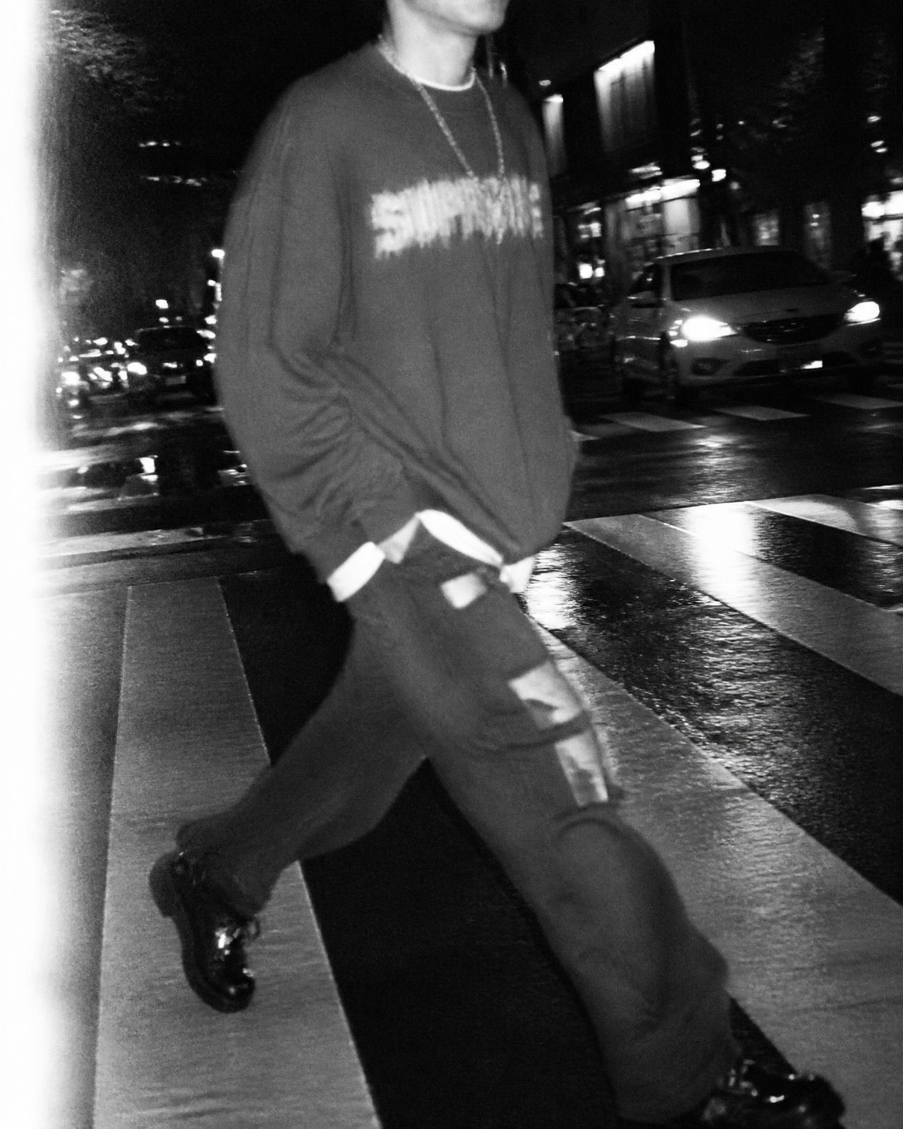 Anonymous figure in oversized streetwear crossing a wet city street at night